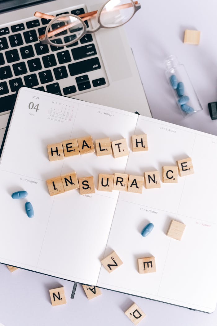 Top view of health insurance planning with scrabble tiles, glasses, and pills.